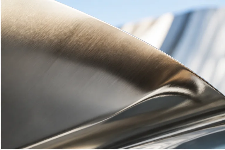 Close-up of a stainless steel sculpture surface reflecting architecture and daylight